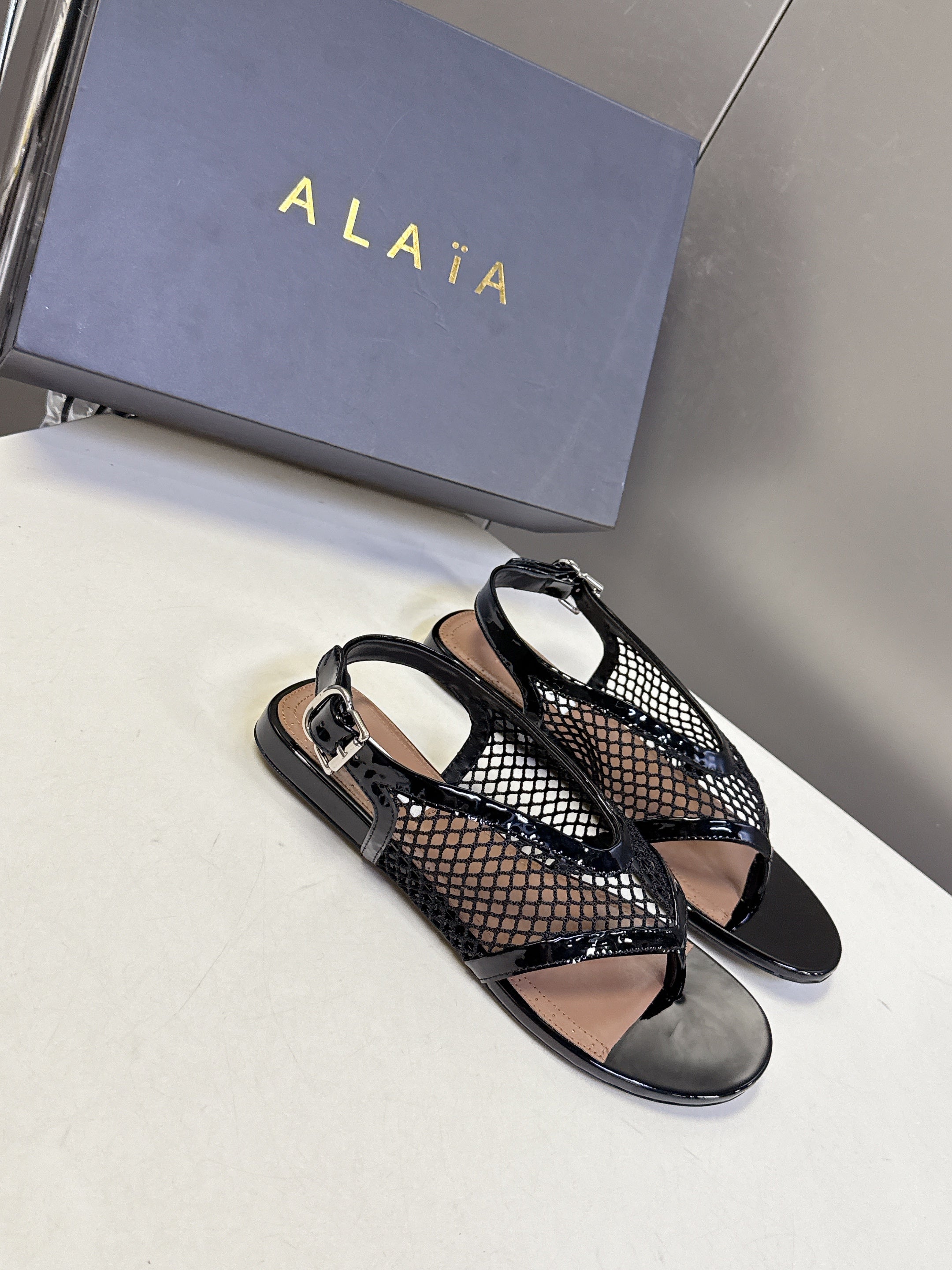 ALAIA 26S FLAT MESH THONG SANDALS IN BLACK PATENT CALFSKIN